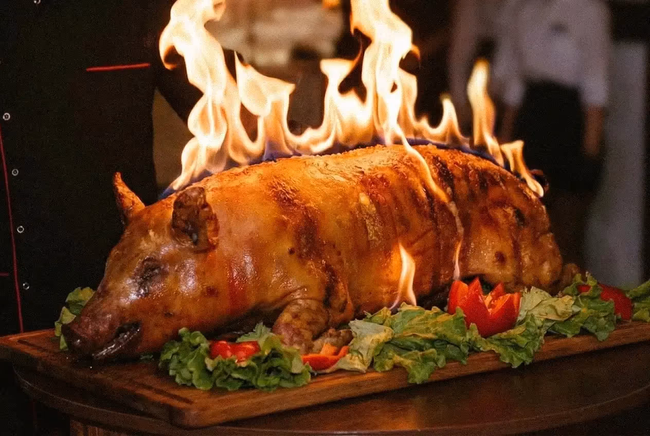 Flambirowany pieczony prosiak na drewnianej desce z warzywami podczas pokazu kulinarnego