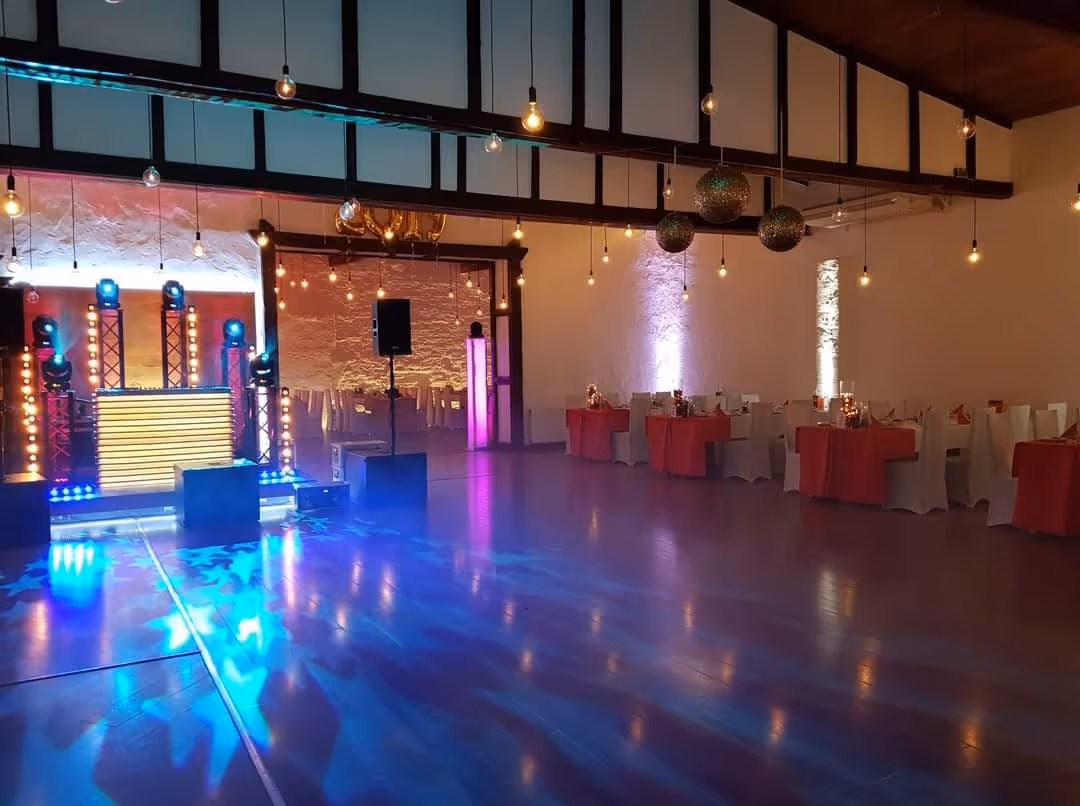 Parkiet z kolorowym oświetleniem disco, kule lustrzane i stoły z czerwonymi obrusami w sali Wrzosowego Tartaku