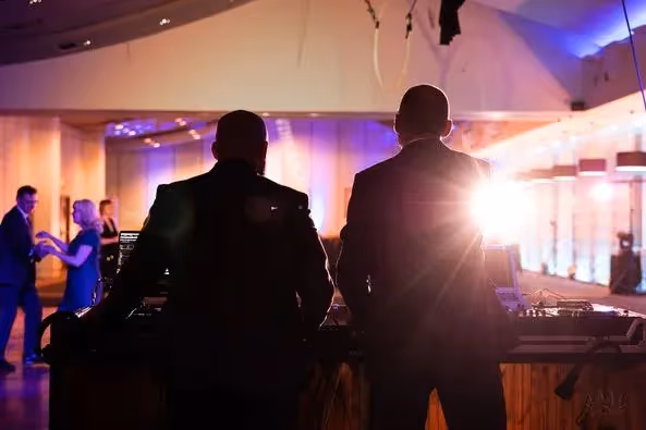 Dwóch DJ-ów za konsoletą na tle fioletowego oświetlenia sali i tańczących gości