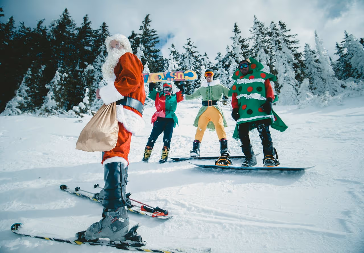 Grupa w przebraniach Mikołaja, elfa i choinki na nartach i snowboardzie na zaśnieżonym stoku